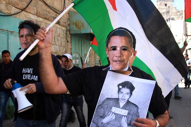 A Palestinian activist wearing a mask of President Barack Obama, holds a Rosa Parks’ mug shot, in the West Bank town of Hebron, on March 20, 2013 [AP]