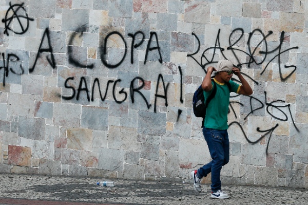  A protester walks by a graffiti that reads in Portuguese "the Cup bleeds," during a demonstration against the 2014 World Cup in Belo Horizonte, Brazil, Thursday, June, 12, 2014 [AP Images]