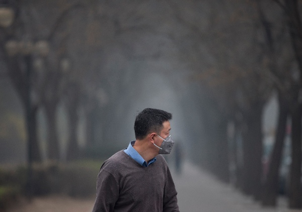 A man wearing a mask walks past trees shrouded with pollution haze in Beijing, China Thursday, March 27, 2014. Air pollution kills about 7 million people worldwide every year according to a new report from the World Health Organization published Tuesday, March 25. The agency said air pollution triggers about 1 in 8 deaths and has now become the single biggest environmental health risk, ahead of other dangers like second-hand smoke [AP]