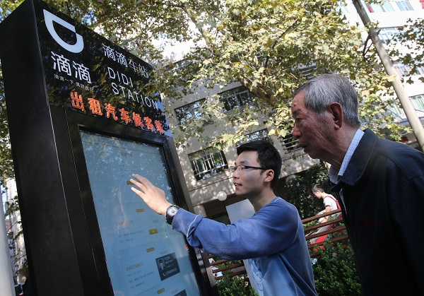 A staff member (L) of Didi Kuaidi, car service Uber's major rival in China, instructs people to order taxis at a Didi station in east China's Shanghai, Oct. 15, 2015 [Xinhua]